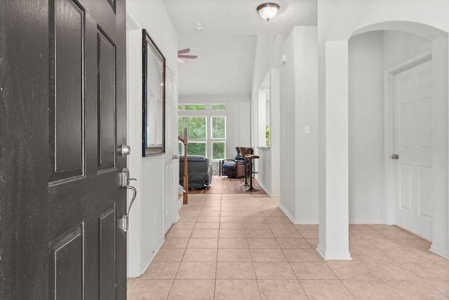 entryway with arched walkways, baseboards, a ceiling fan, and light tile patterned flooring