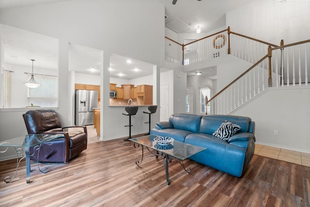 living room featuring stairway, baseboards, a high ceiling, and light wood-type flooring