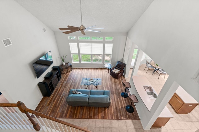 living area featuring baseboards, a ceiling fan, a textured ceiling, and visible vents