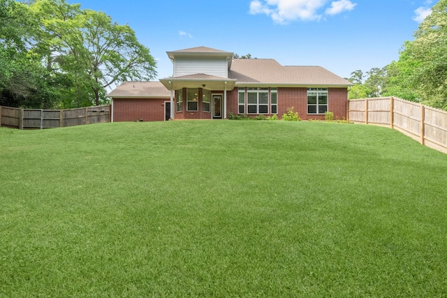 rear view of property with a yard, brick siding, and a fenced backyard