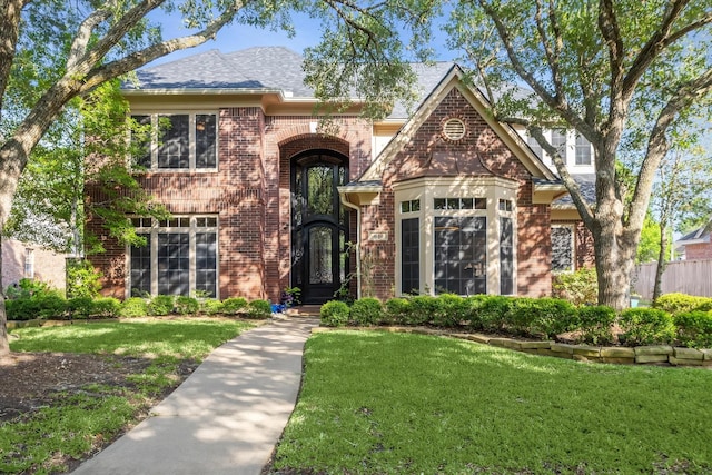 traditional-style home featuring roof with shingles, a front lawn, and brick siding