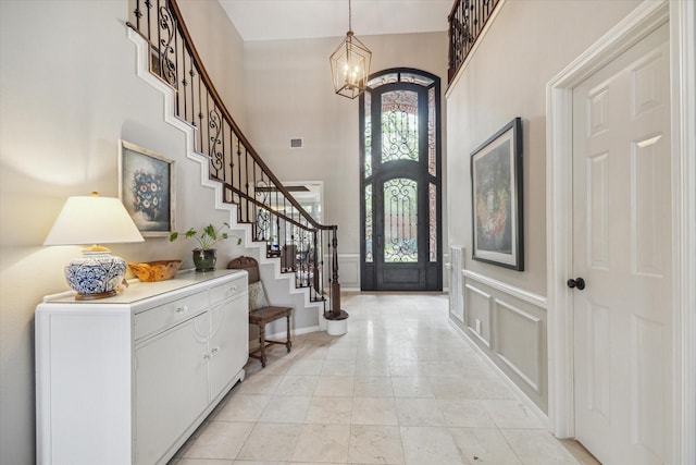 foyer with visible vents, stairs, a decorative wall, a high ceiling, and a chandelier