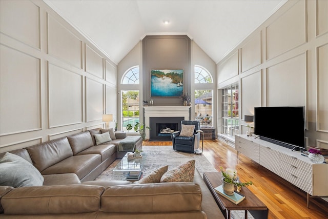 living room featuring a fireplace with flush hearth, light wood finished floors, a decorative wall, and high vaulted ceiling
