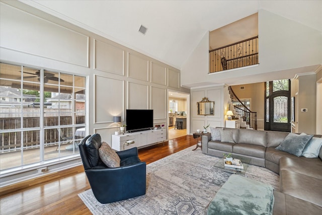 living room featuring high vaulted ceiling, a decorative wall, stairs, and wood finished floors