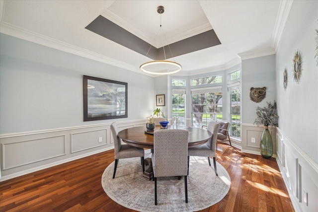 dining room featuring crown molding, a decorative wall, a wainscoted wall, wood finished floors, and a tray ceiling