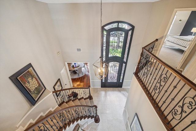 foyer entrance featuring visible vents, tile patterned flooring, a towering ceiling, baseboards, and a chandelier