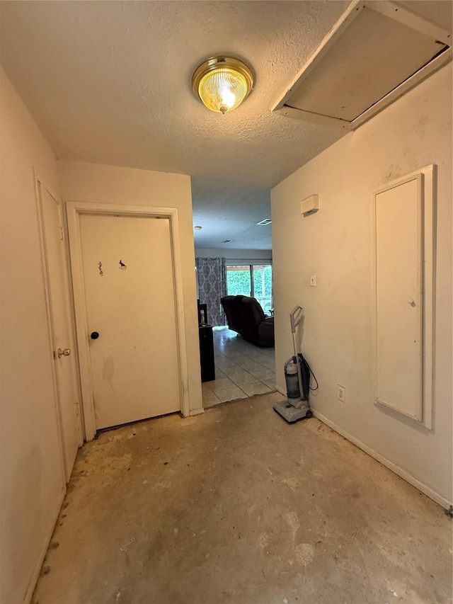 hallway featuring concrete flooring, a textured ceiling, and attic access