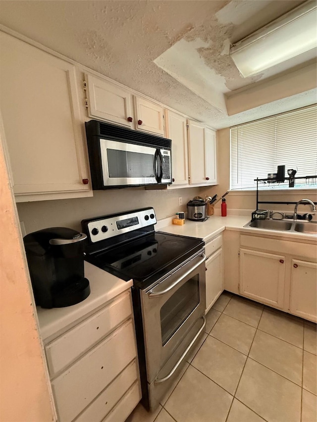 kitchen featuring light countertops, white cabinets, a sink, appliances with stainless steel finishes, and light tile patterned floors