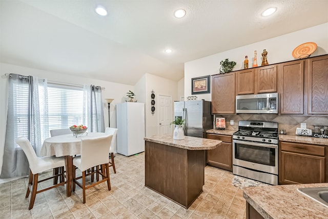 kitchen featuring decorative backsplash, a kitchen island, vaulted ceiling, light countertops, and stainless steel appliances
