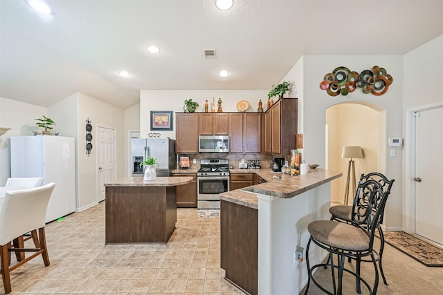kitchen featuring appliances with stainless steel finishes, a breakfast bar, light countertops, a center island, and backsplash