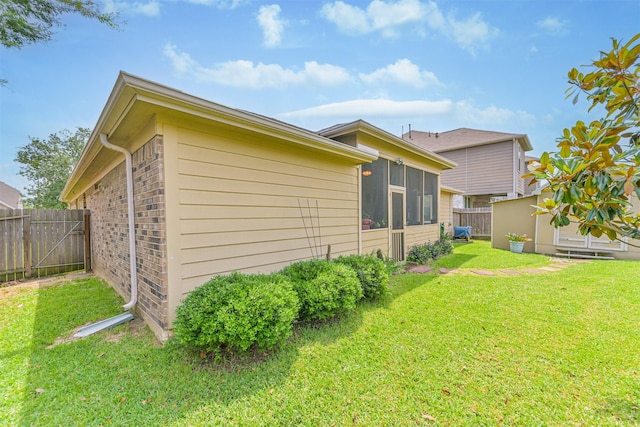 view of side of property featuring a fenced backyard, a yard, a storage unit, a sunroom, and an outbuilding