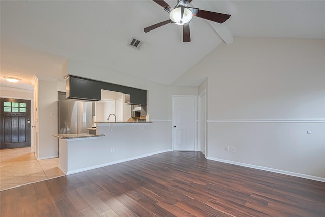 unfurnished living room featuring ceiling fan, visible vents, wood finished floors, baseboards, and lofted ceiling with beams