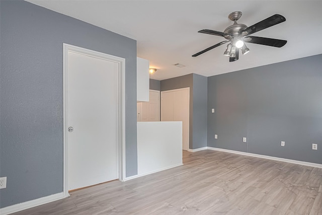 empty room with light wood-type flooring, a ceiling fan, and baseboards