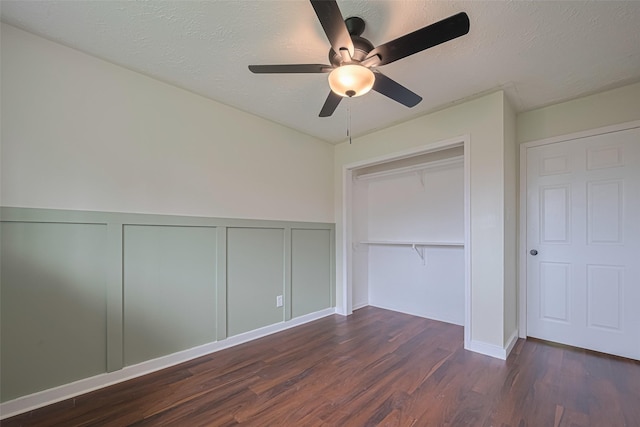 unfurnished bedroom featuring ceiling fan, wainscoting, wood finished floors, a closet, and a decorative wall