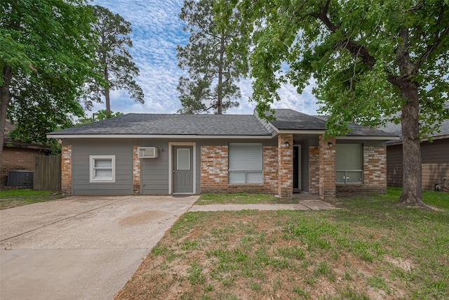 ranch-style house featuring fence, a shingled roof, central AC, brick siding, and a wall mounted air conditioner