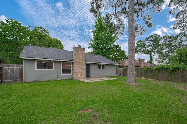 back of house featuring a chimney, a lawn, a fenced backyard, a patio, and a shingled roof