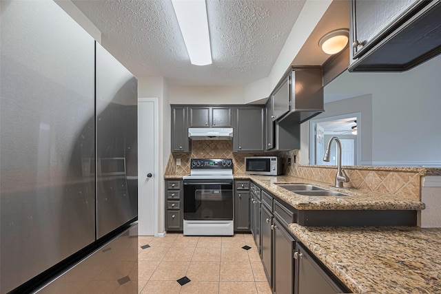 kitchen with light stone countertops, under cabinet range hood, a sink, appliances with stainless steel finishes, and backsplash