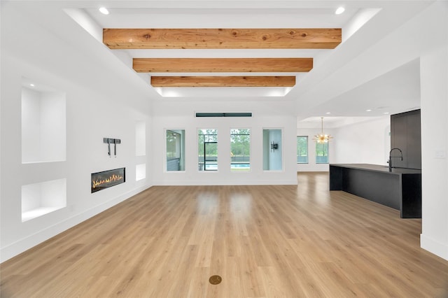 unfurnished living room with light wood-style flooring, a glass covered fireplace, beam ceiling, and a notable chandelier
