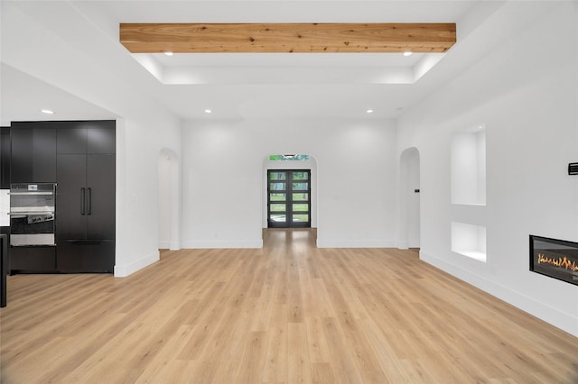 unfurnished living room featuring light wood-style floors, arched walkways, a glass covered fireplace, and recessed lighting