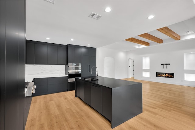 kitchen with a sink, light wood-style floors, dark cabinetry, visible vents, and modern cabinets