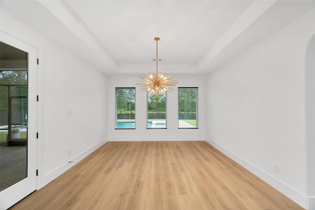 unfurnished room with baseboards, light wood-style flooring, a raised ceiling, and a chandelier