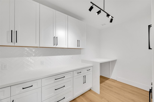kitchen with backsplash, rail lighting, light countertops, light wood-style floors, and white cabinetry