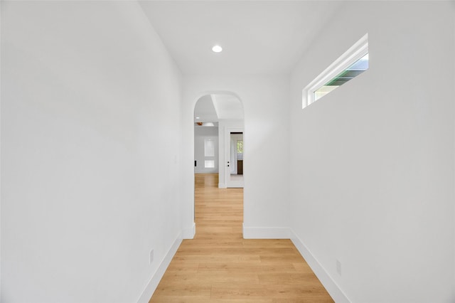 corridor with arched walkways, baseboards, recessed lighting, and light wood-type flooring