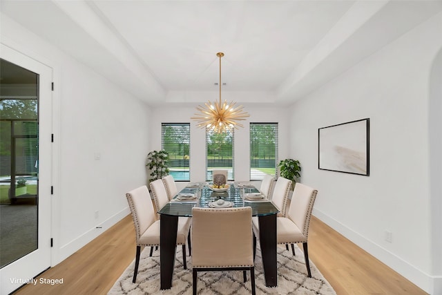 dining space with an inviting chandelier, baseboards, a tray ceiling, and light wood-type flooring