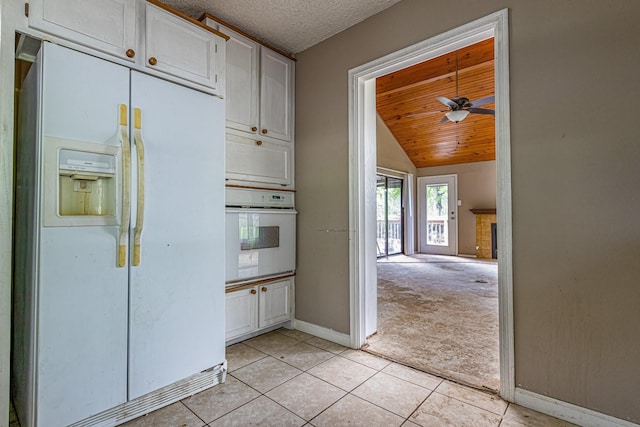 kitchen featuring light colored carpet, baseboards, lofted ceiling, white appliances, and light tile patterned flooring