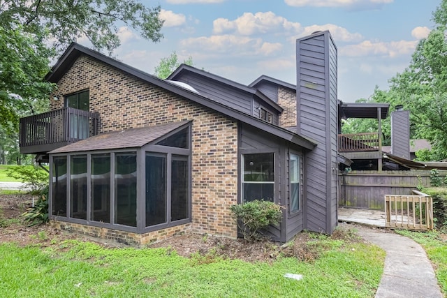 back of house featuring a sunroom, a chimney, brick siding, and fence