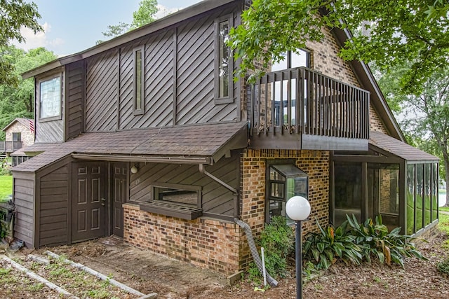 back of house with a balcony, a sunroom, roof with shingles, and brick siding