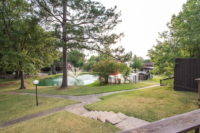 view of property's community featuring a lawn, a water view, and fence