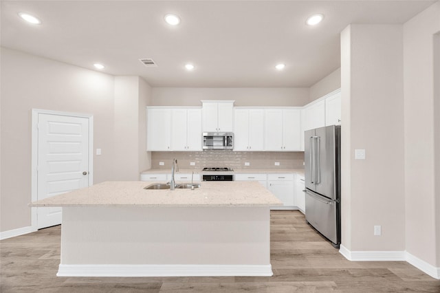 kitchen with appliances with stainless steel finishes, a sink, light wood-style floors, an island with sink, and tasteful backsplash