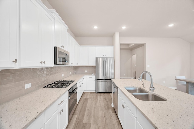 kitchen featuring light stone countertops, white cabinetry, a sink, light wood-style flooring, and stainless steel appliances