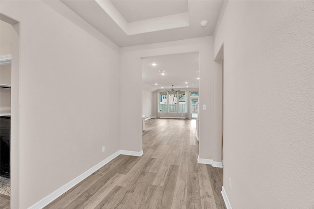 hallway with recessed lighting, baseboards, light wood-style flooring, and a tray ceiling