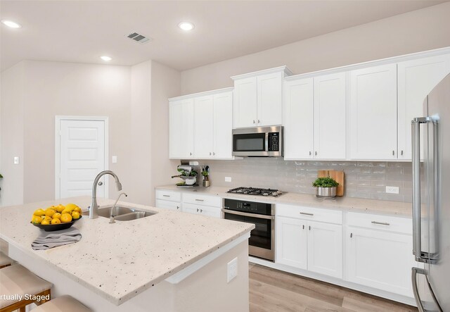 kitchen featuring decorative backsplash, visible vents, a sink, stainless steel appliances, and white cabinetry