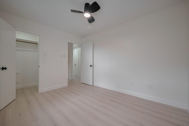 unfurnished bedroom with a walk in closet, baseboards, a ceiling fan, and light wood-style flooring
