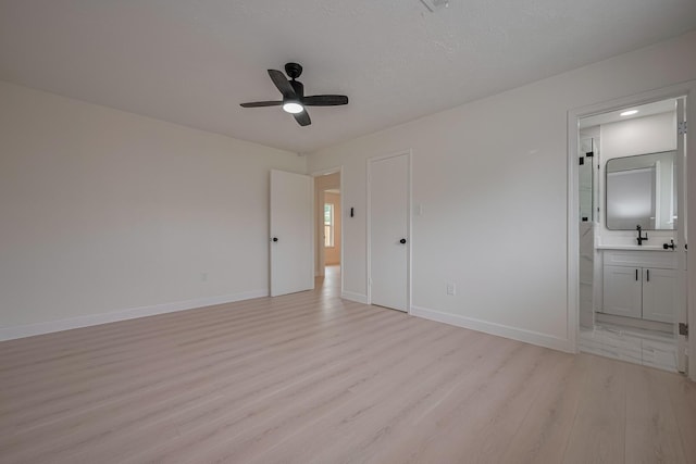unfurnished bedroom with baseboards, ceiling fan, a sink, light wood-style flooring, and ensuite bath