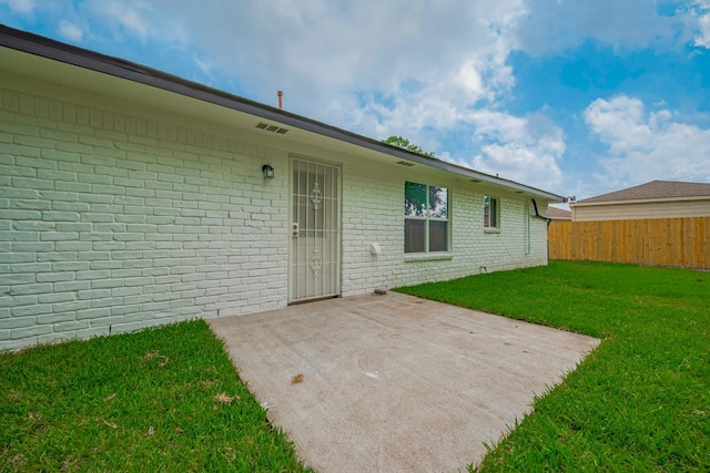 view of exterior entry featuring fence, a yard, a patio area, and brick siding