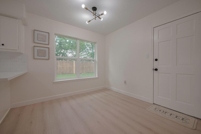 unfurnished dining area featuring an inviting chandelier, baseboards, and light wood finished floors