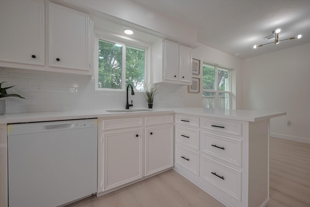 kitchen featuring a sink, dishwasher, light countertops, a peninsula, and decorative backsplash
