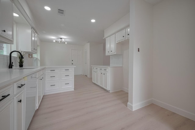 kitchen with a sink, a peninsula, light wood-type flooring, tasteful backsplash, and visible vents