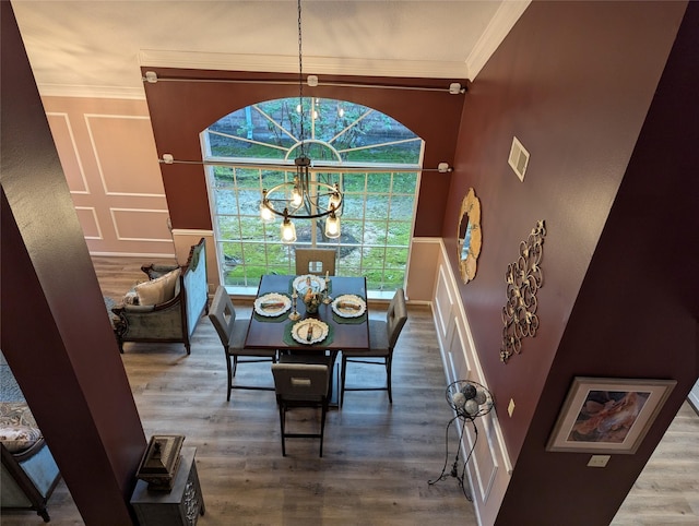dining space with a chandelier, crown molding, wood finished floors, and a wainscoted wall