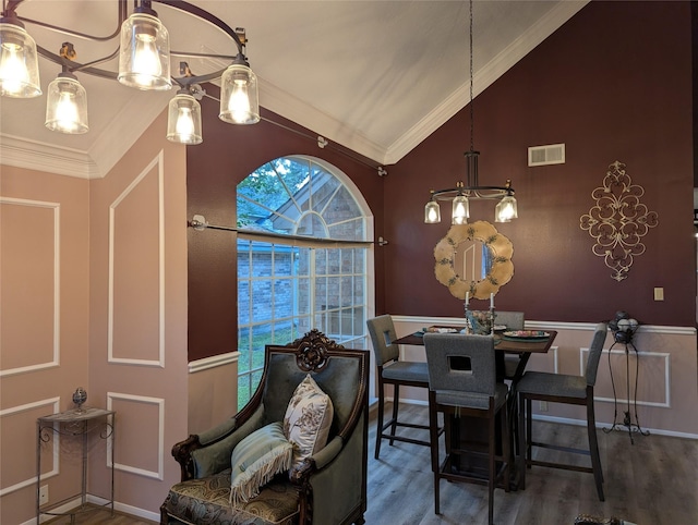 dining space featuring lofted ceiling, wood finished floors, ornamental molding, and a wainscoted wall
