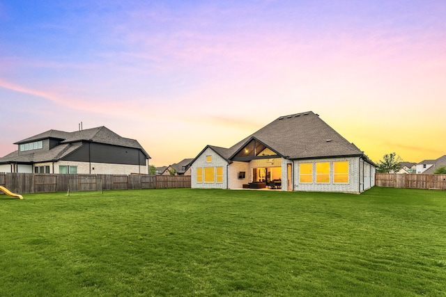 back of house at dusk featuring a lawn, a fenced backyard, a patio area, and brick siding