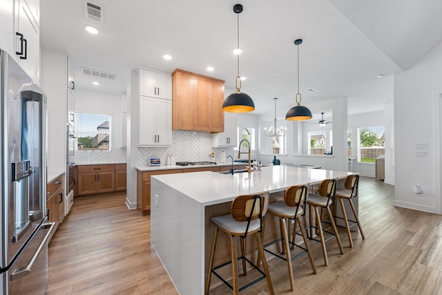 kitchen with a sink, appliances with stainless steel finishes, a center island with sink, and visible vents