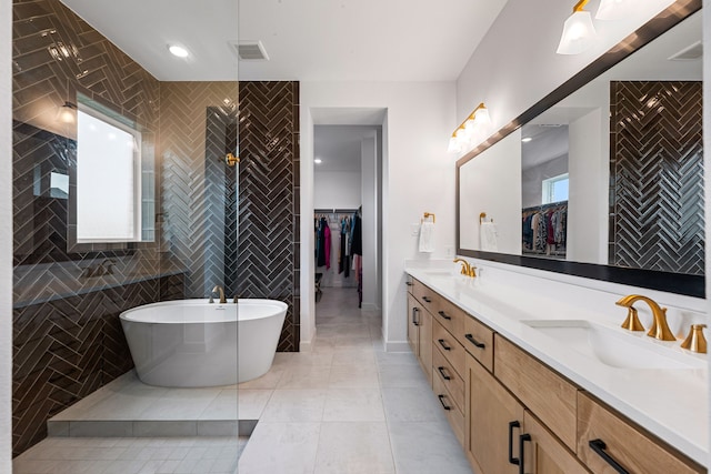 full bath featuring double vanity, tile walls, a walk in closet, a soaking tub, and a sink
