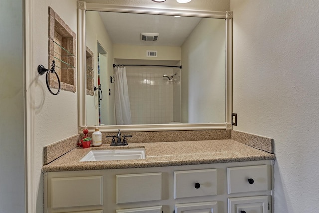 full bath featuring vanity, a textured wall, visible vents, and a shower with shower curtain