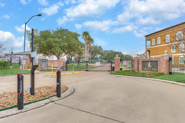 view of street featuring a gate, a gated entry, curbs, and street lighting