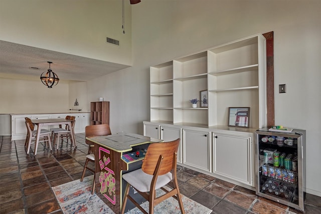 dining space featuring visible vents, beverage cooler, a high ceiling, stone finish floor, and a chandelier